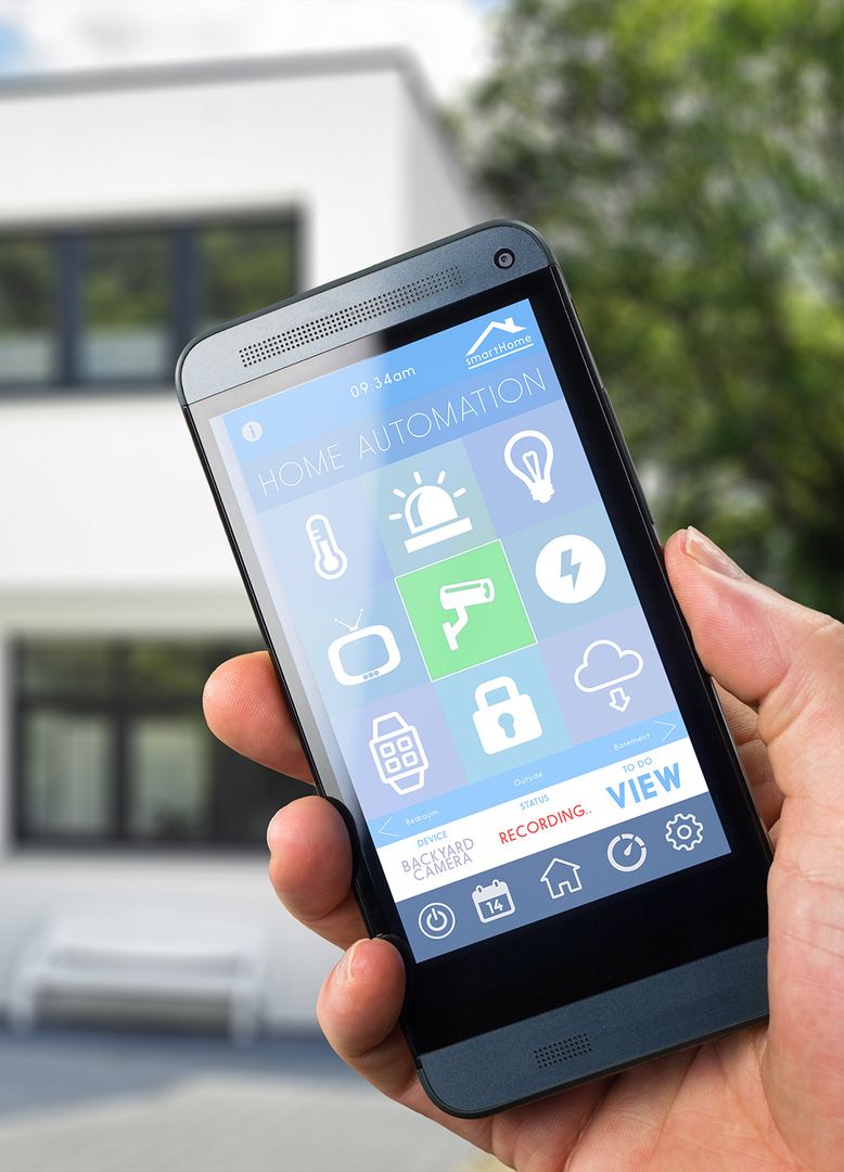 Eine Hand hält ein Smartphone, auf diesem sieht man verschieden Buttons bzgl. Smart Home